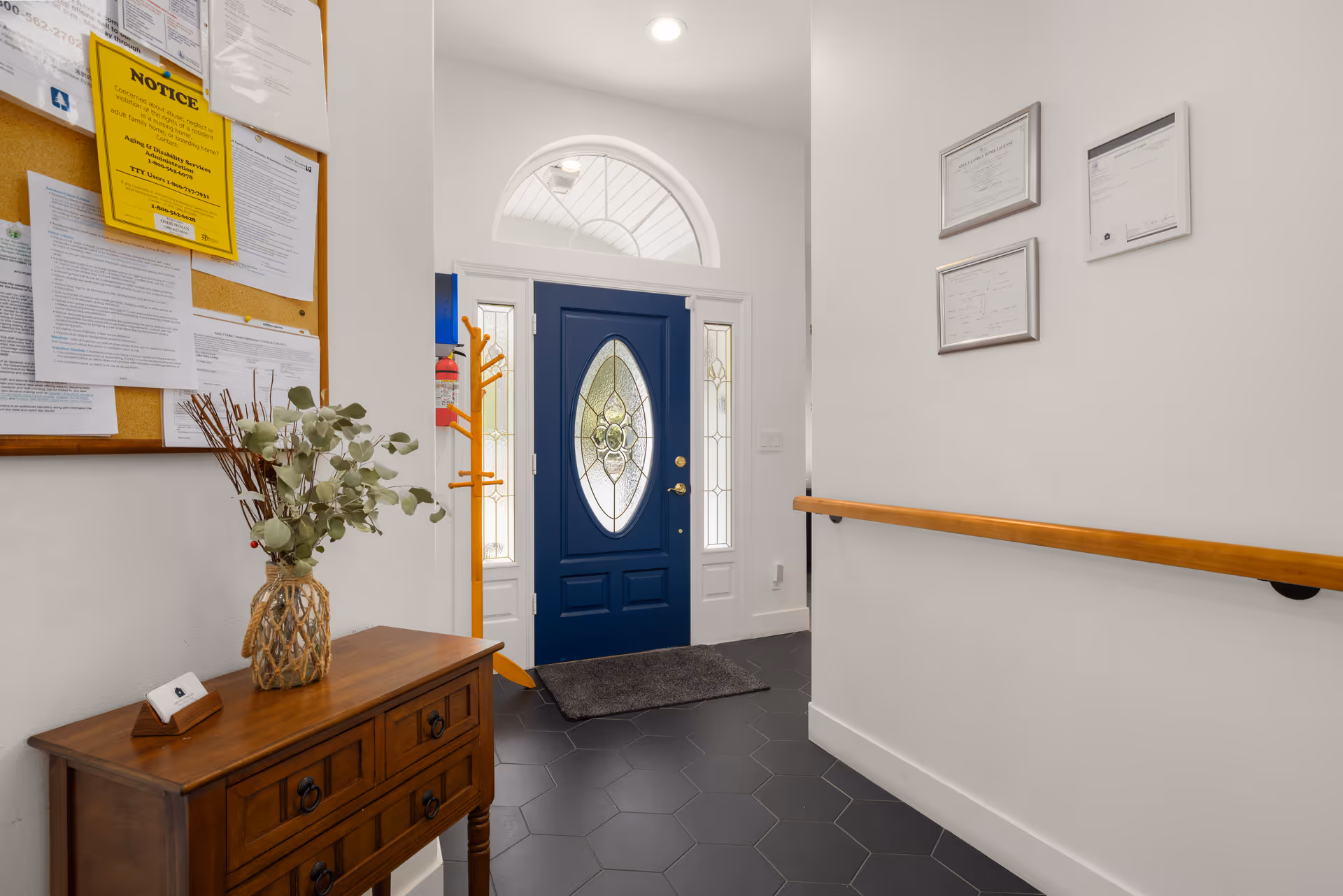 Bright interior entry hall with a blue front door, hex tile floor, and wall certificates.