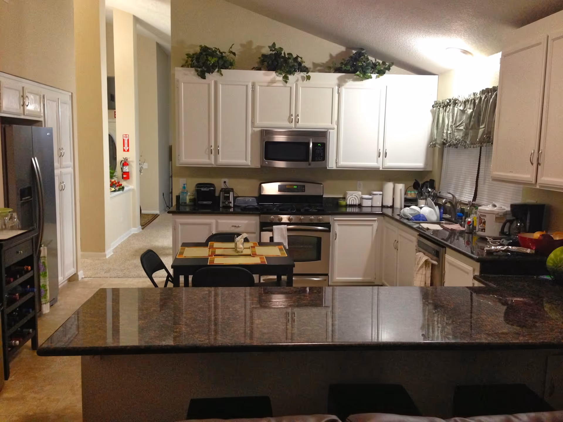 Bright kitchen with white cabinets, stainless appliances, granite island, and a small dining table.