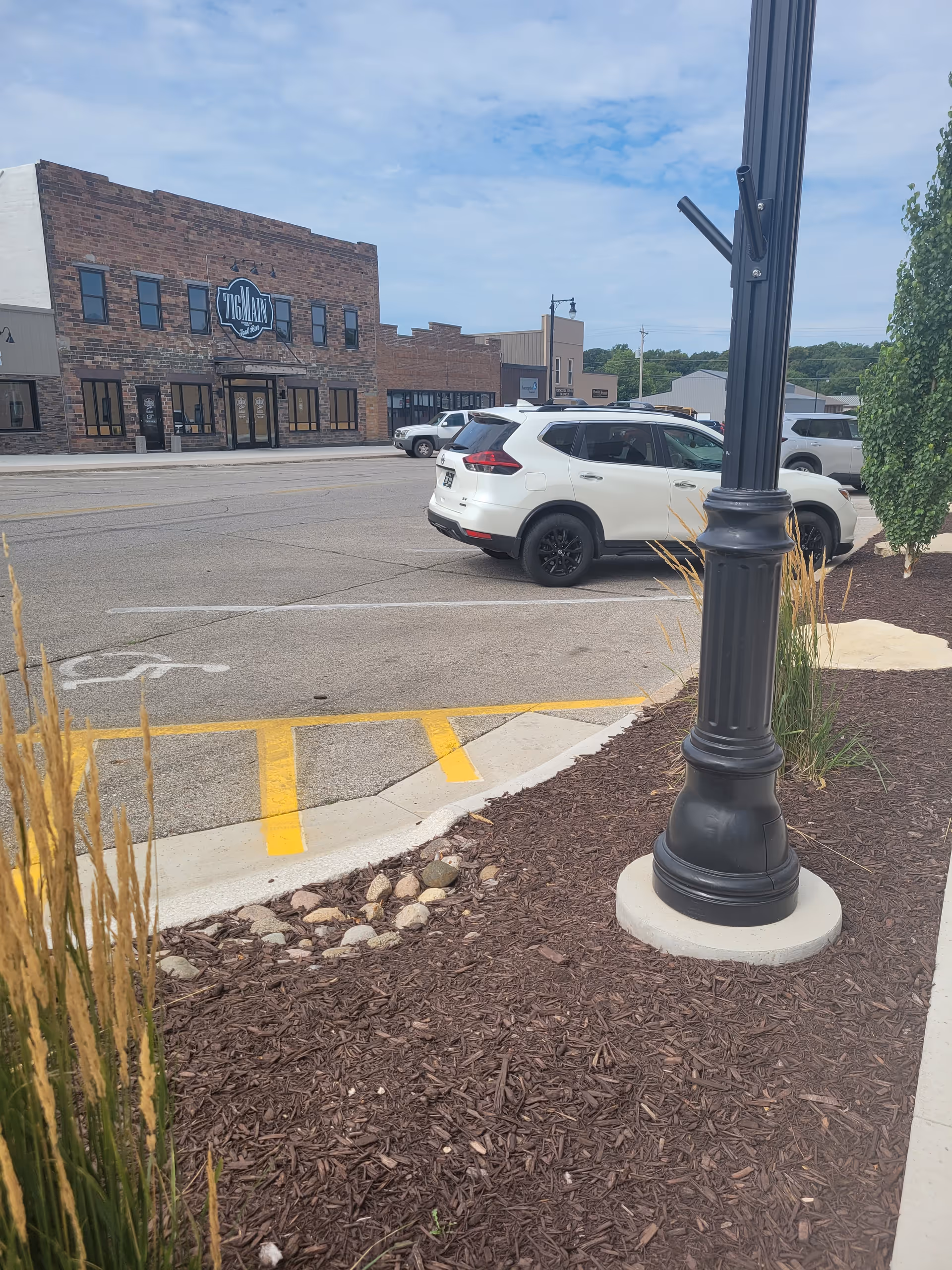 Empty parking lot and brick storefronts with a tall street lamp in foreground.