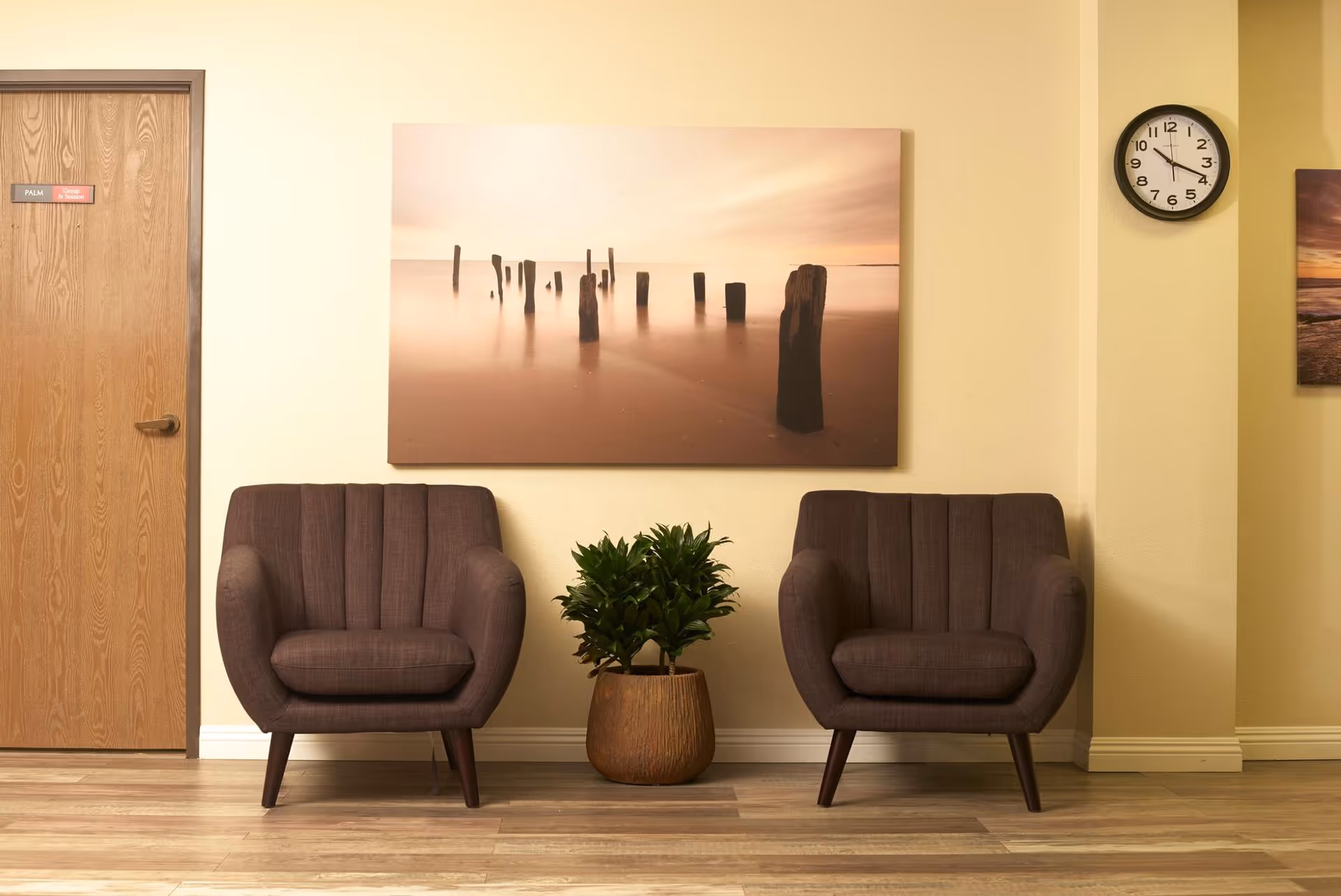 Two purple chairs flank a potted plant in a beige lobby with wall art.