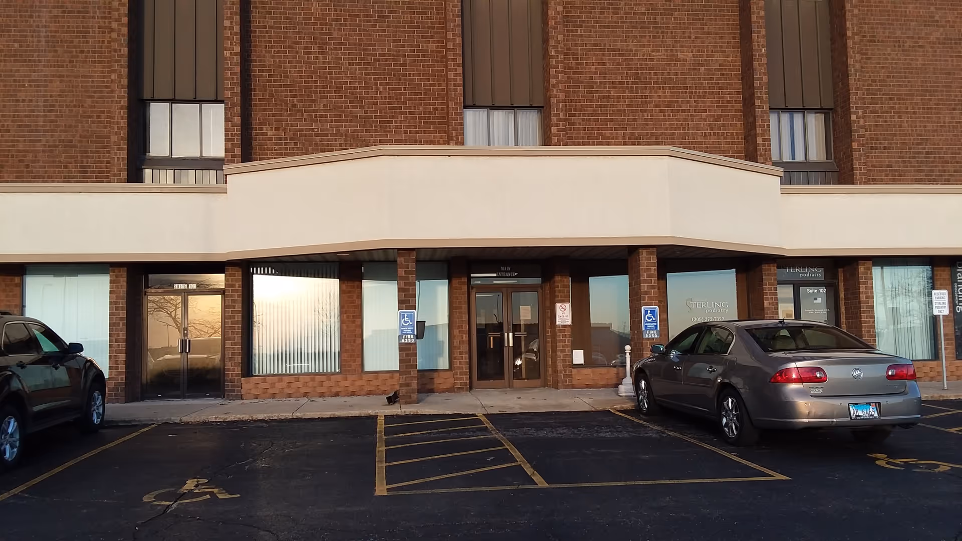 Brick senior living facility entrance with glass doors and parked cars.