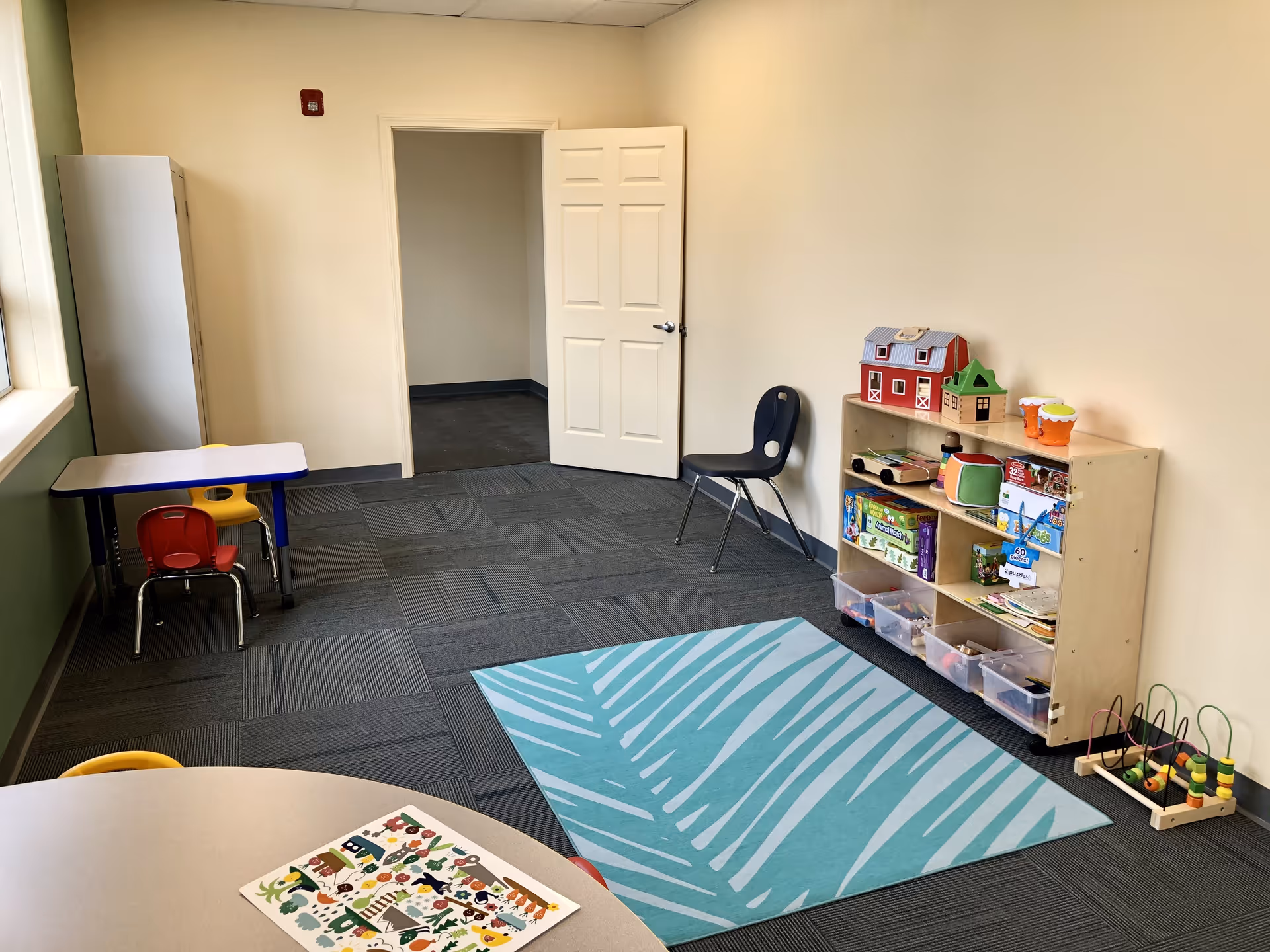 Bright activity room with toy shelves, small tables, chairs, and a zebra-pattern rug.