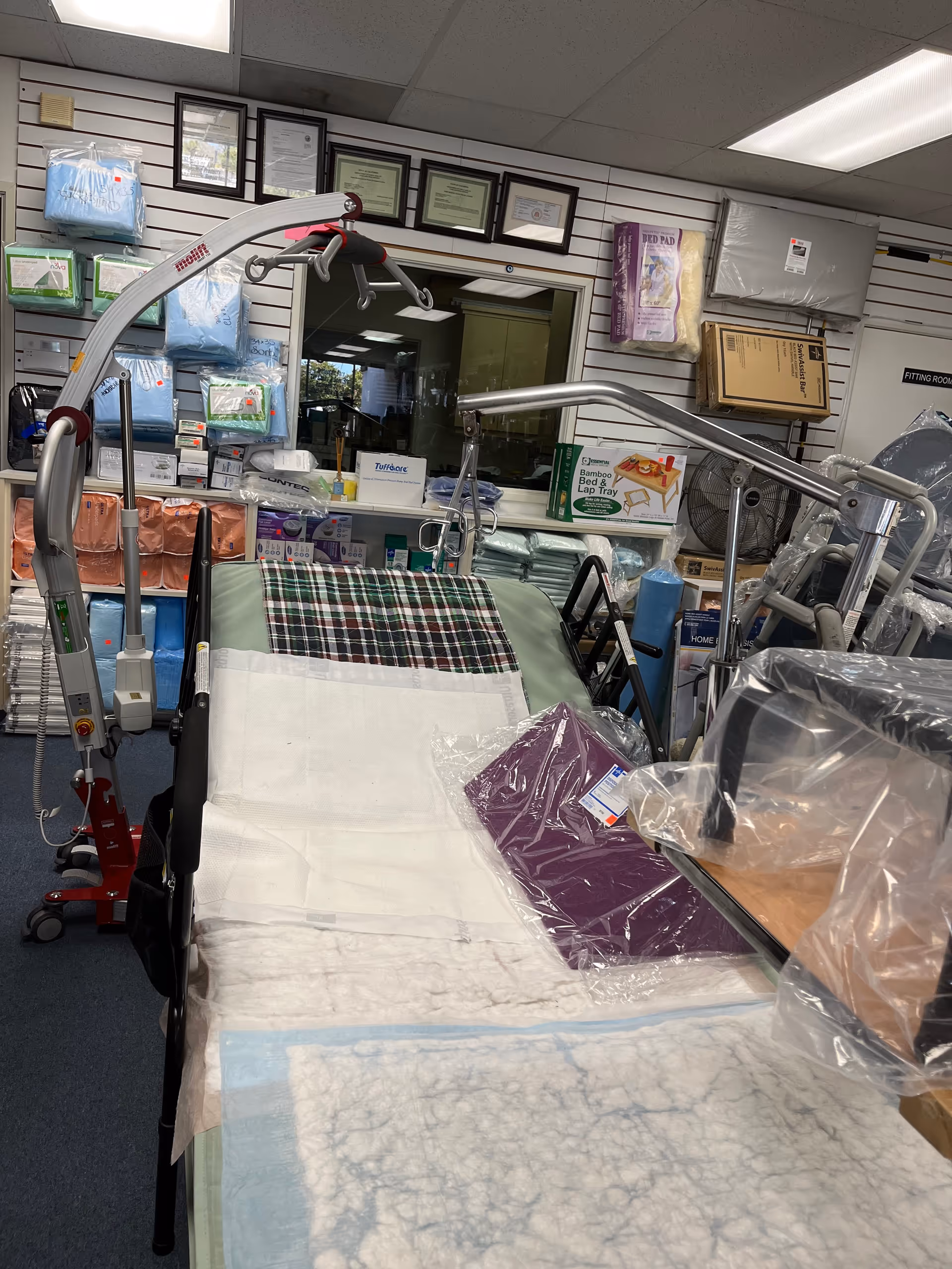 Medical supply room featuring a hospital bed, stacked supplies, and framed certificates on wall.