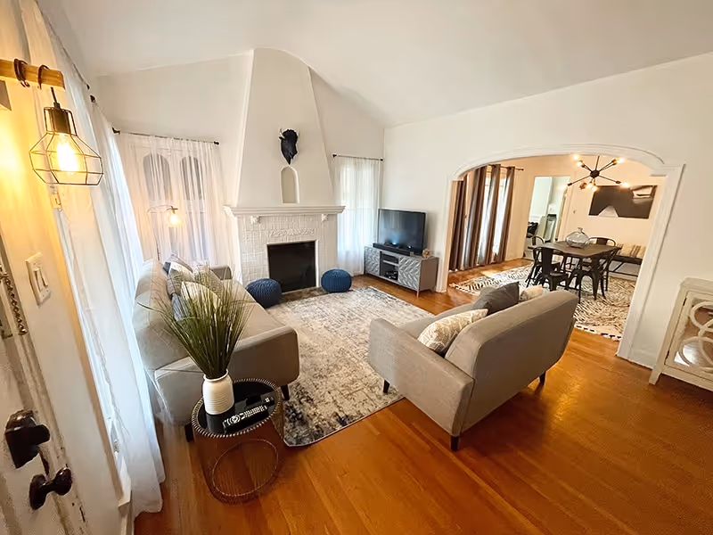 Bright living room with two gray sofas, a fireplace, rug, and adjacent dining area.