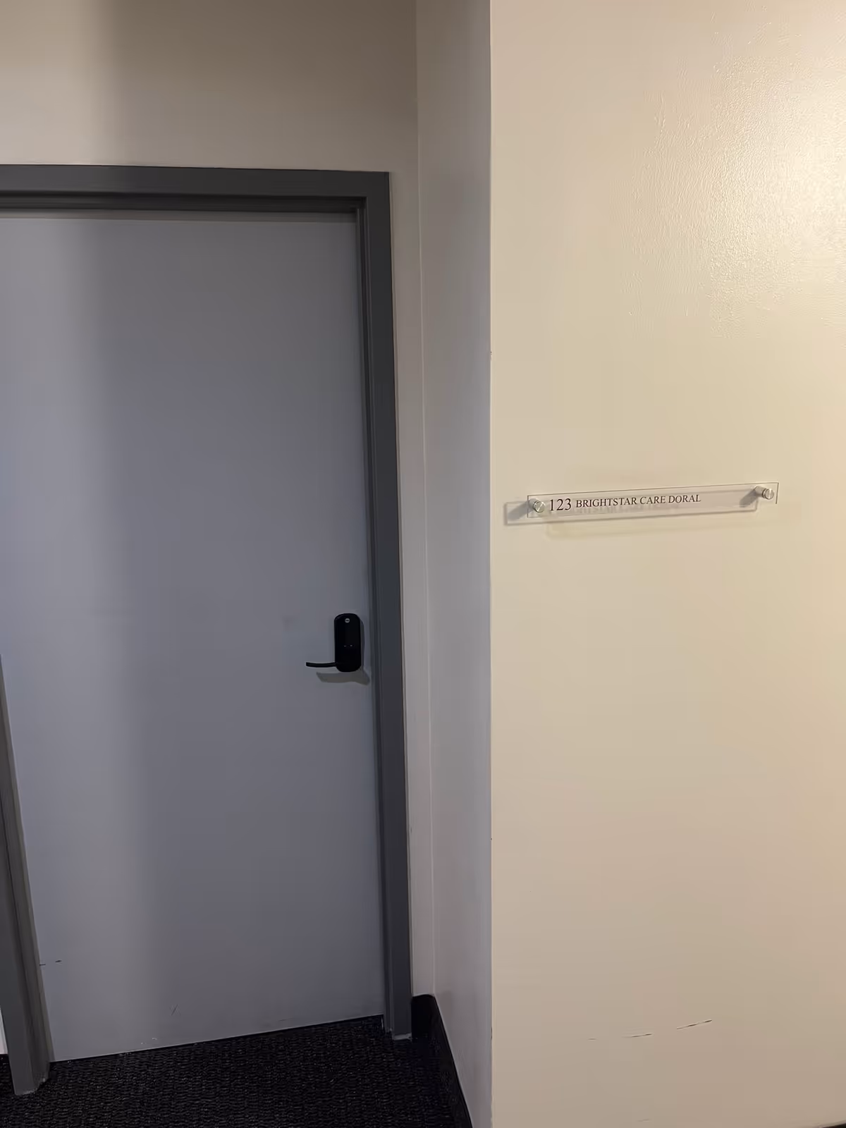 Interior hallway with a closed gray door and a wall plaque labeled 123 BrightStar Care Doral