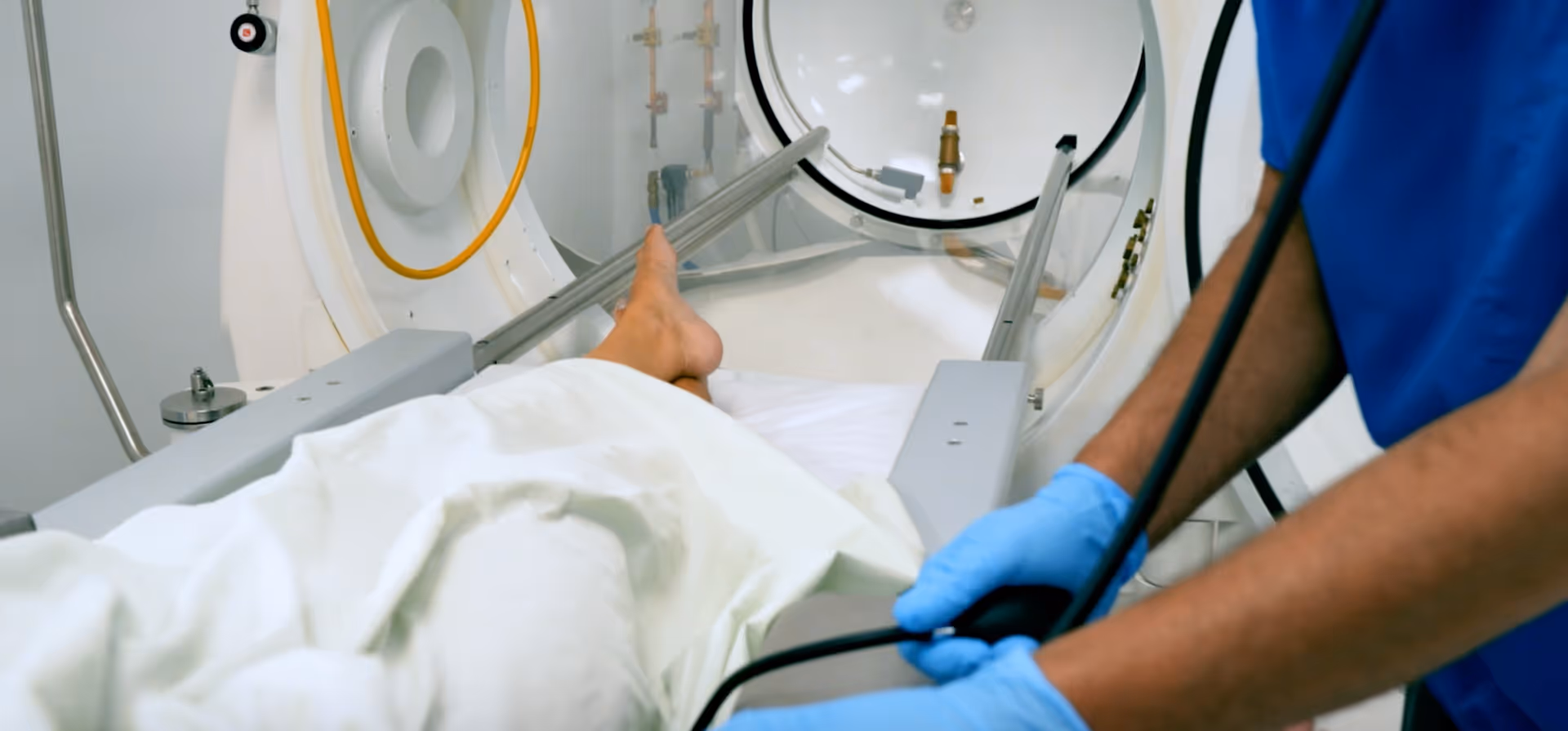 Medical professional in blue gloves assists a patient inside a large medical imaging device.