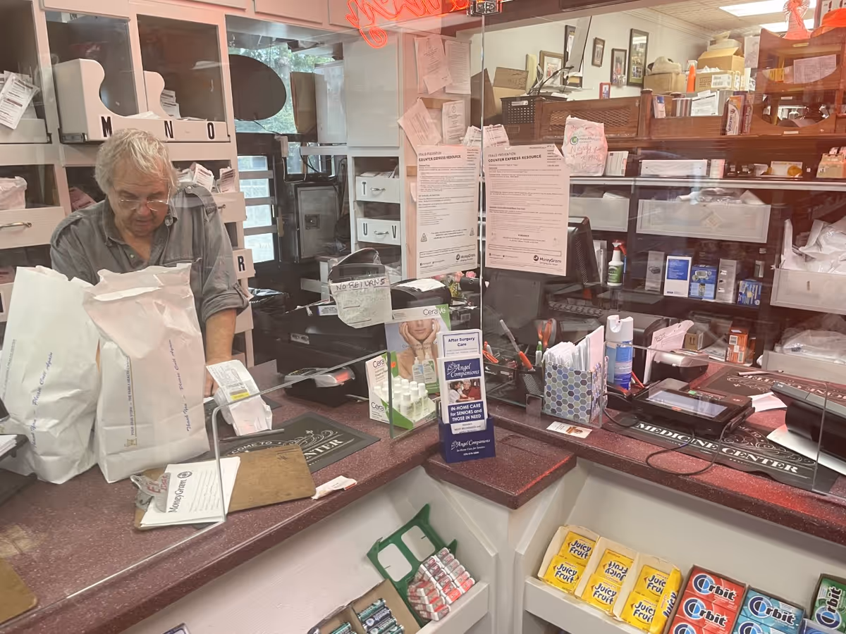 Older man behind a counter sorting mail in a busy reception area.