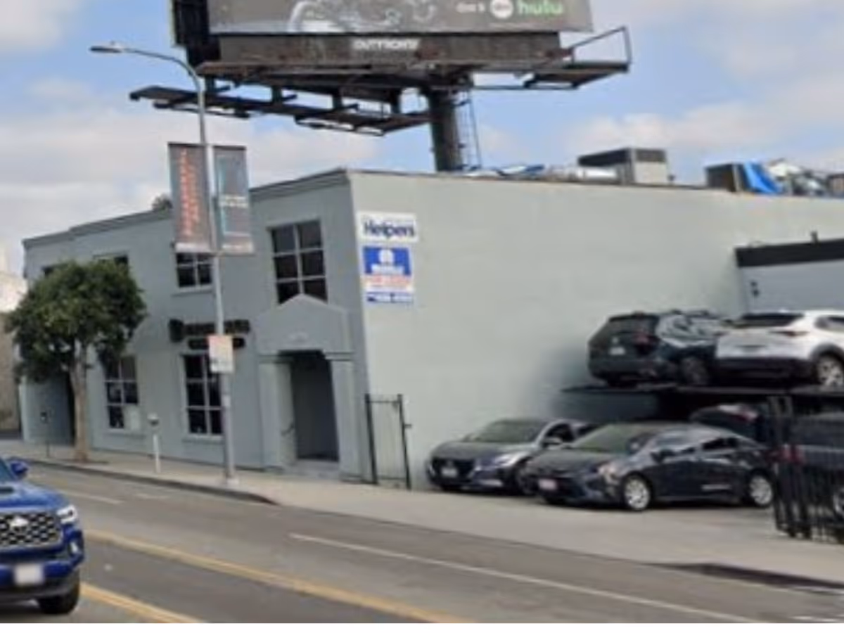 Exterior view of a light gray building on a street with parked cars and a billboard.