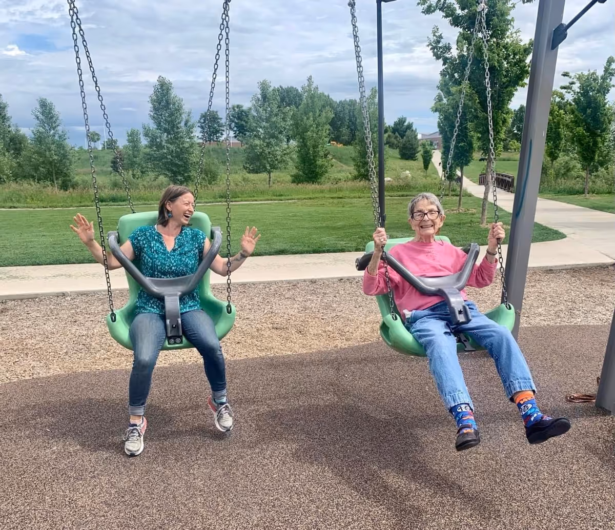 Two people on green swings laugh together in an outdoor park.