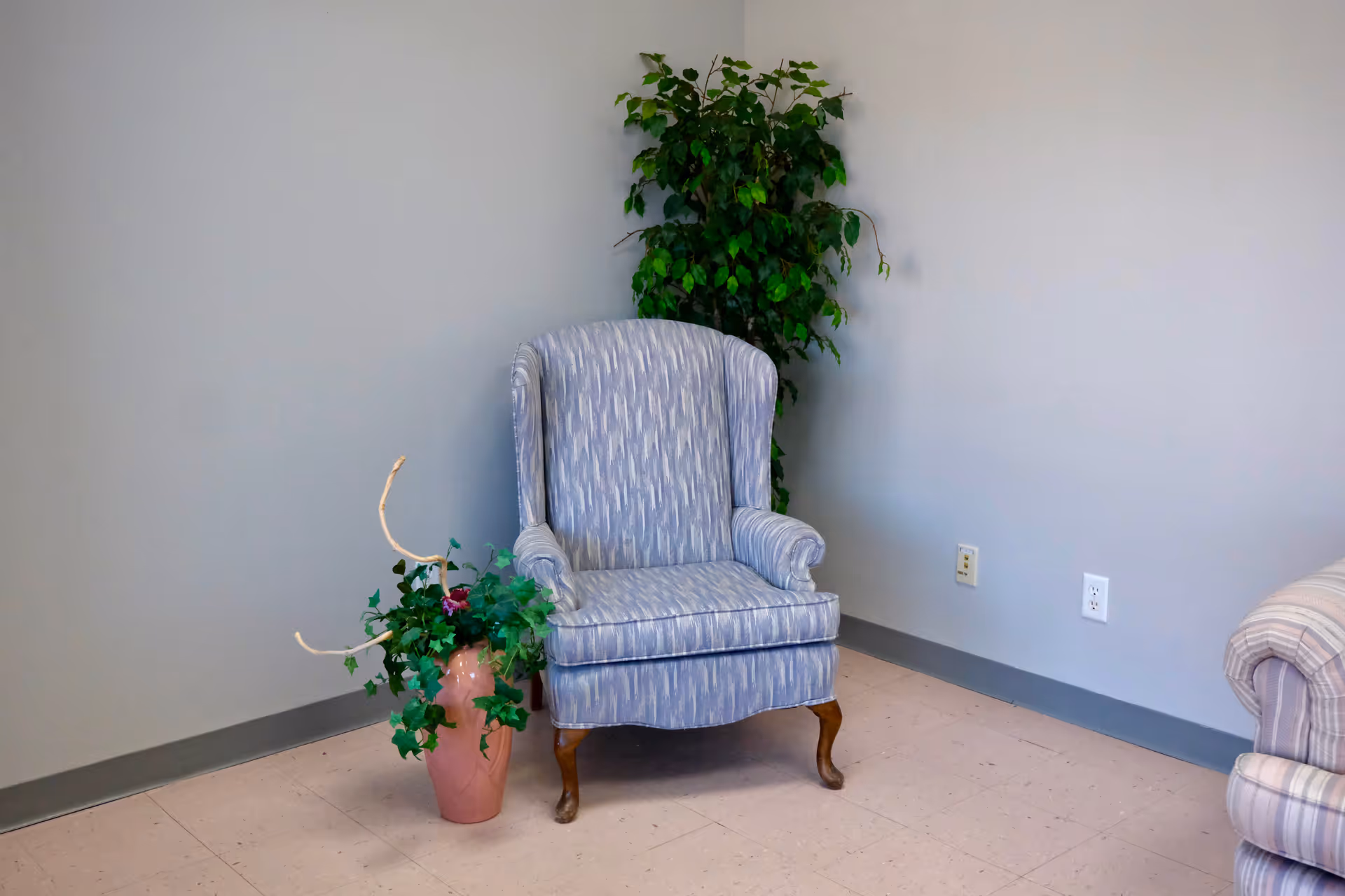 Blue upholstered armchair beside a tall plant in a quiet interior corner.