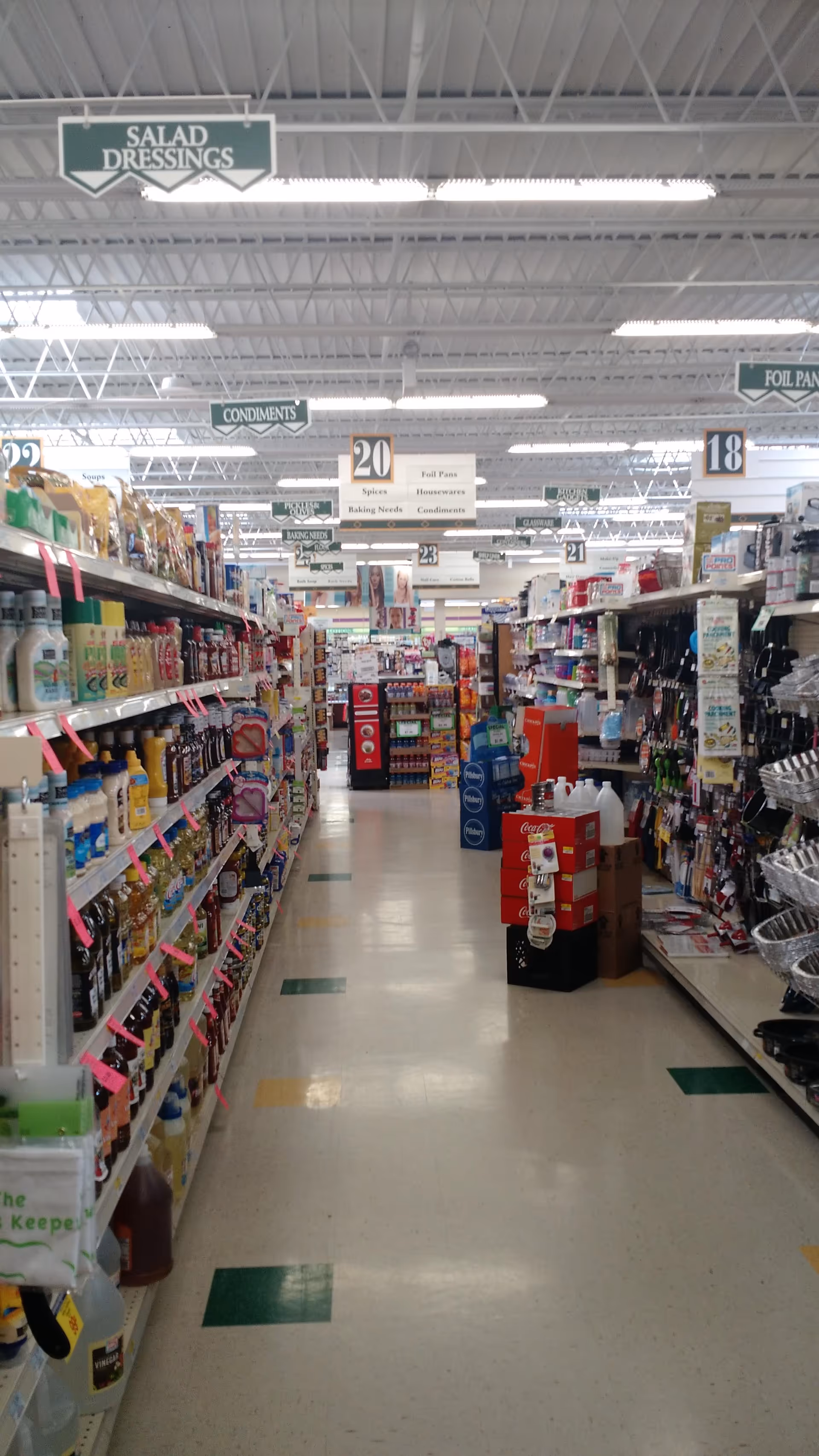 Long drugstore aisle with shelves of condiments and cleaning products under bright lights.