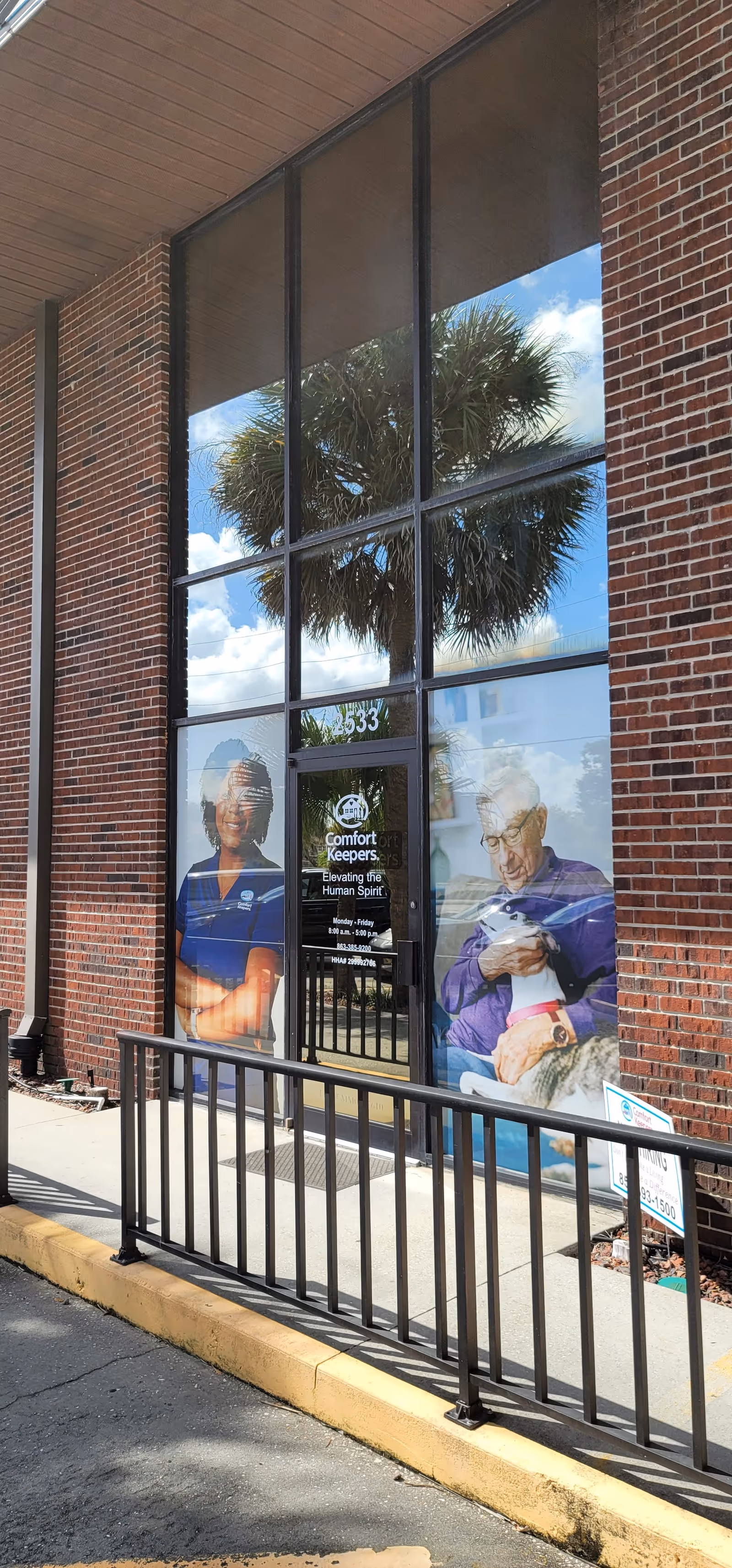 Brick building exterior with large glass entrance doors and posters advertising Comfort Keepers.