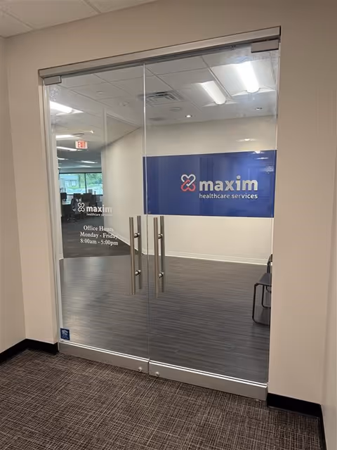 Glass double doors lead to a Maxim Healthcare Services office with a blue logo wall.