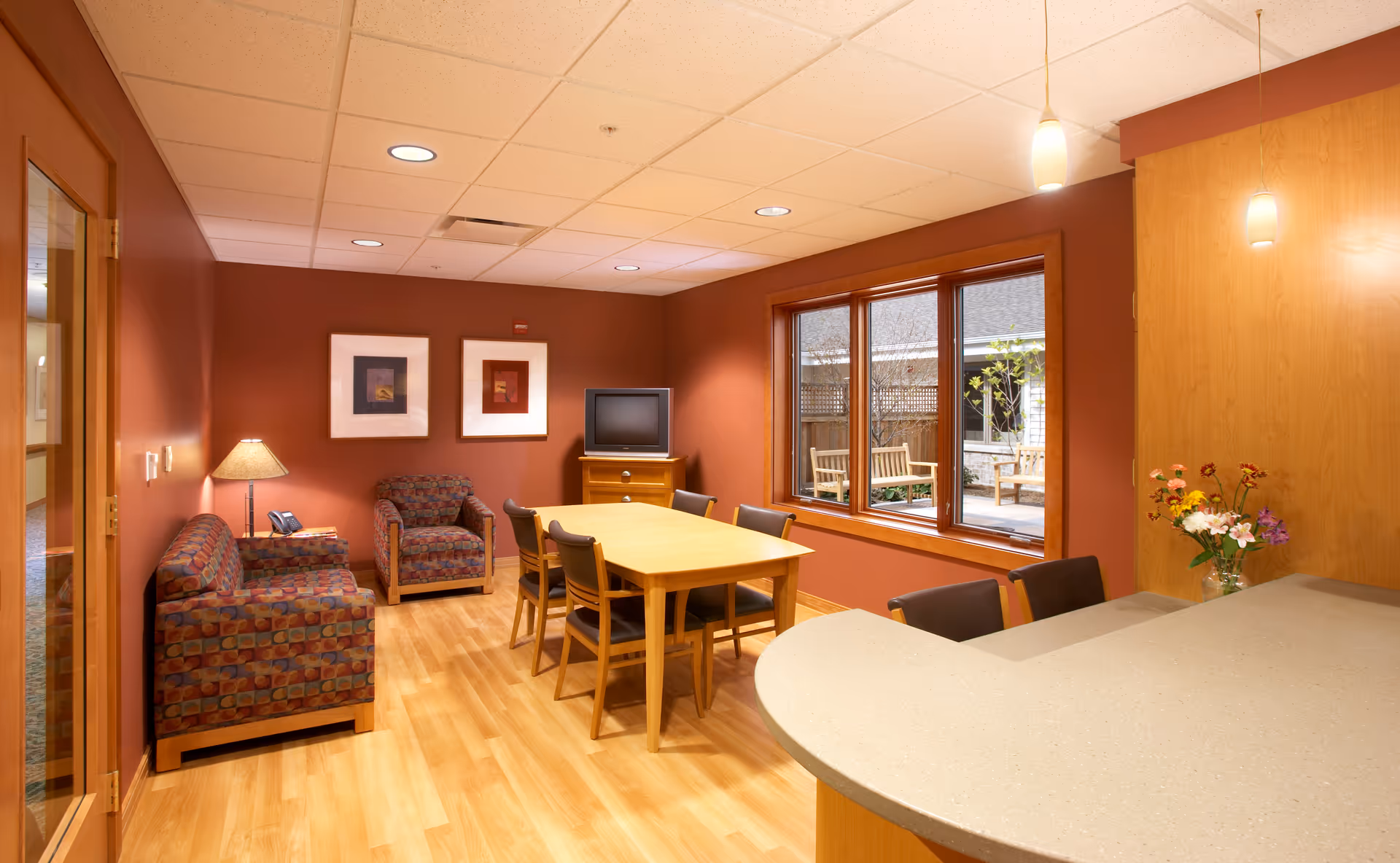 Interior common area with a dining table, seating, a curved counter, and an outdoor patio visible.