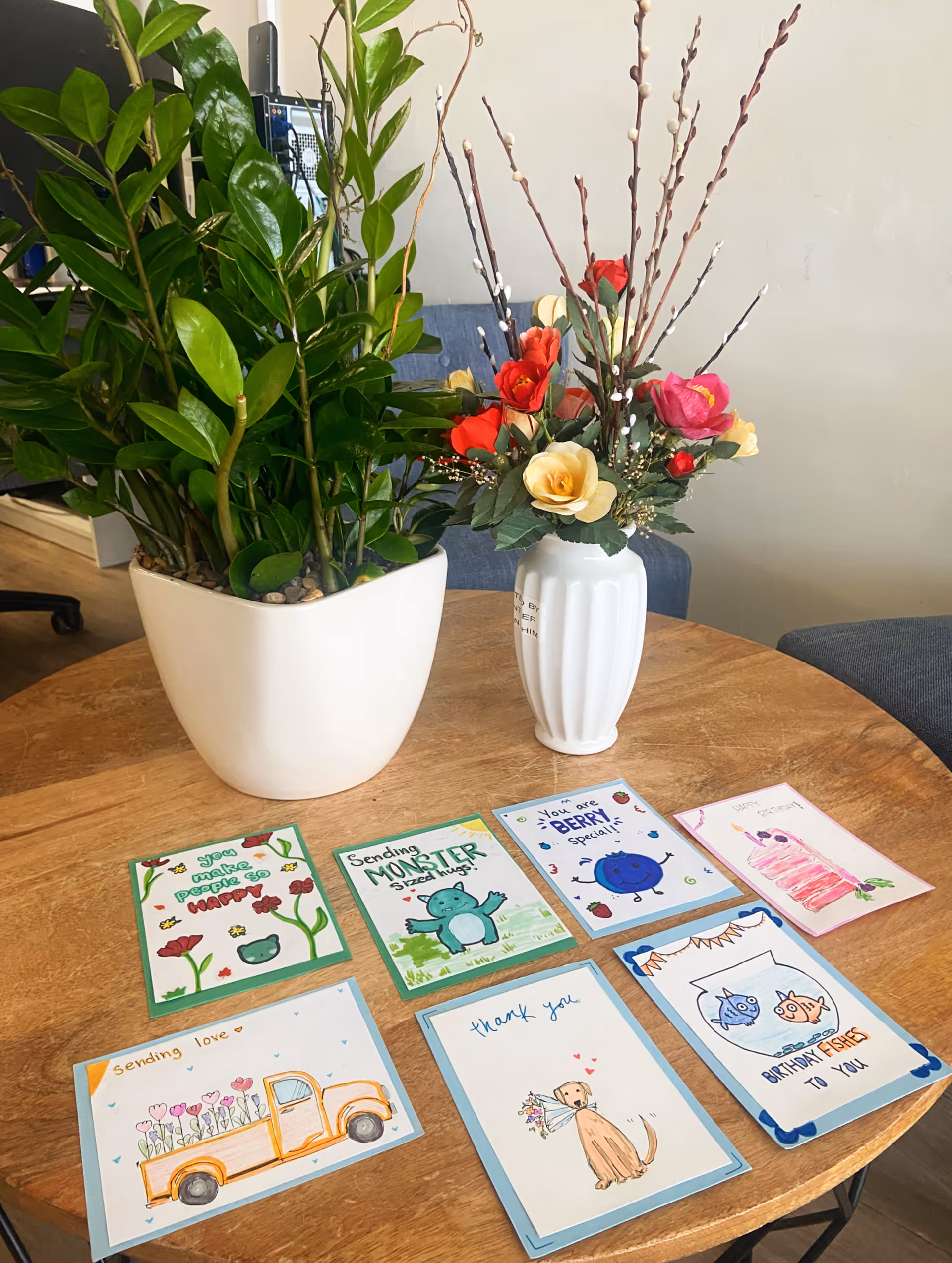 Indoor table with assorted handmade cards and potted plants in a lounge area.