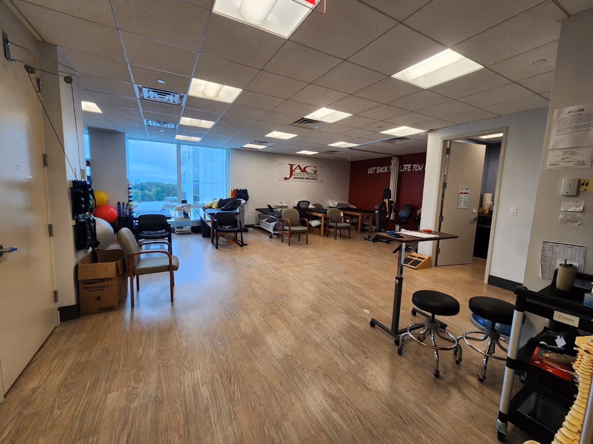 Interior therapy room with exercise equipment, chairs, and a windowed wall in a JAG facility.