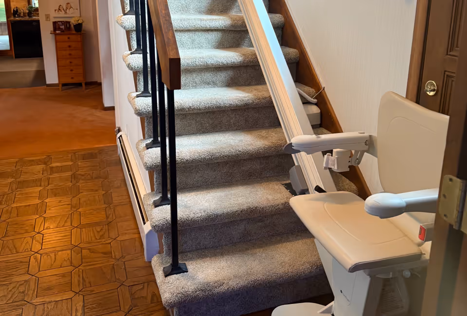 Indoor stairway with carpeted steps and a stairlift chair attached to the railing.