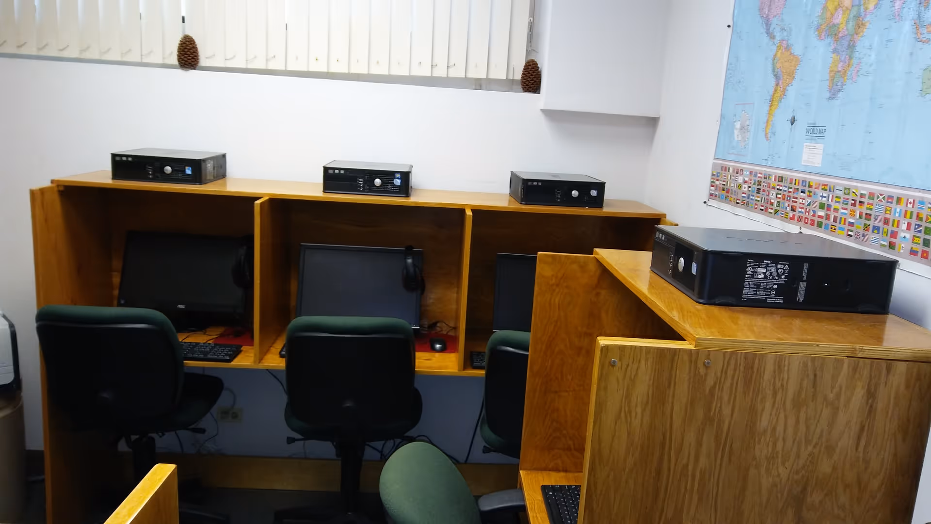 A computer lab with wooden cubicles, monitors, keyboards, and a world map on the wall.