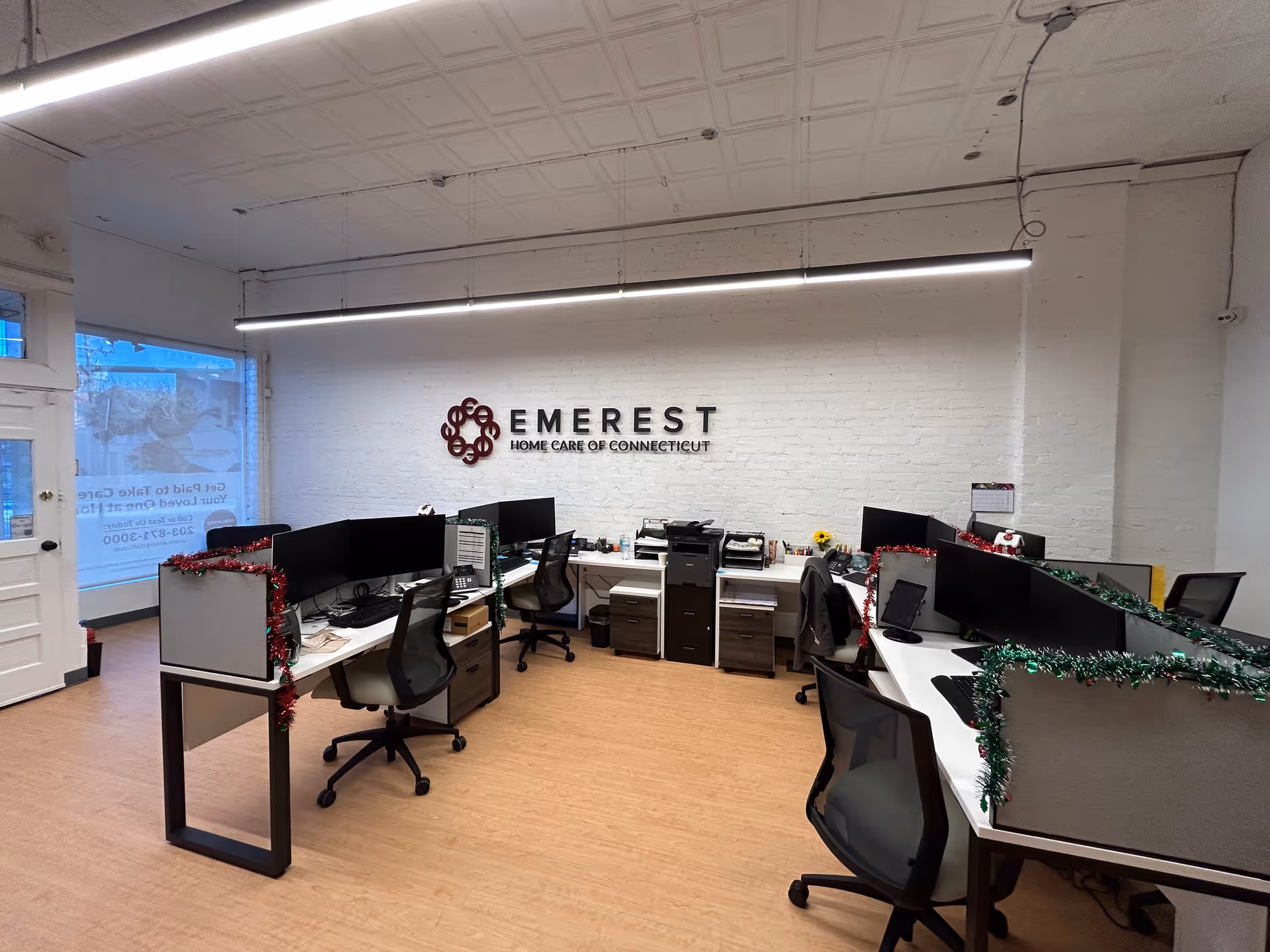 Open office with cubicles, desks, computers, and a wall sign reading EMEREST Home Care.