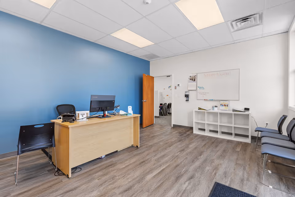 Reception desk with computer, blue wall, and row of chairs in a facility lobby.
