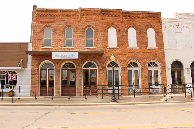 Brick storefront with arched windows and a Visiting Angels sign on the facade.