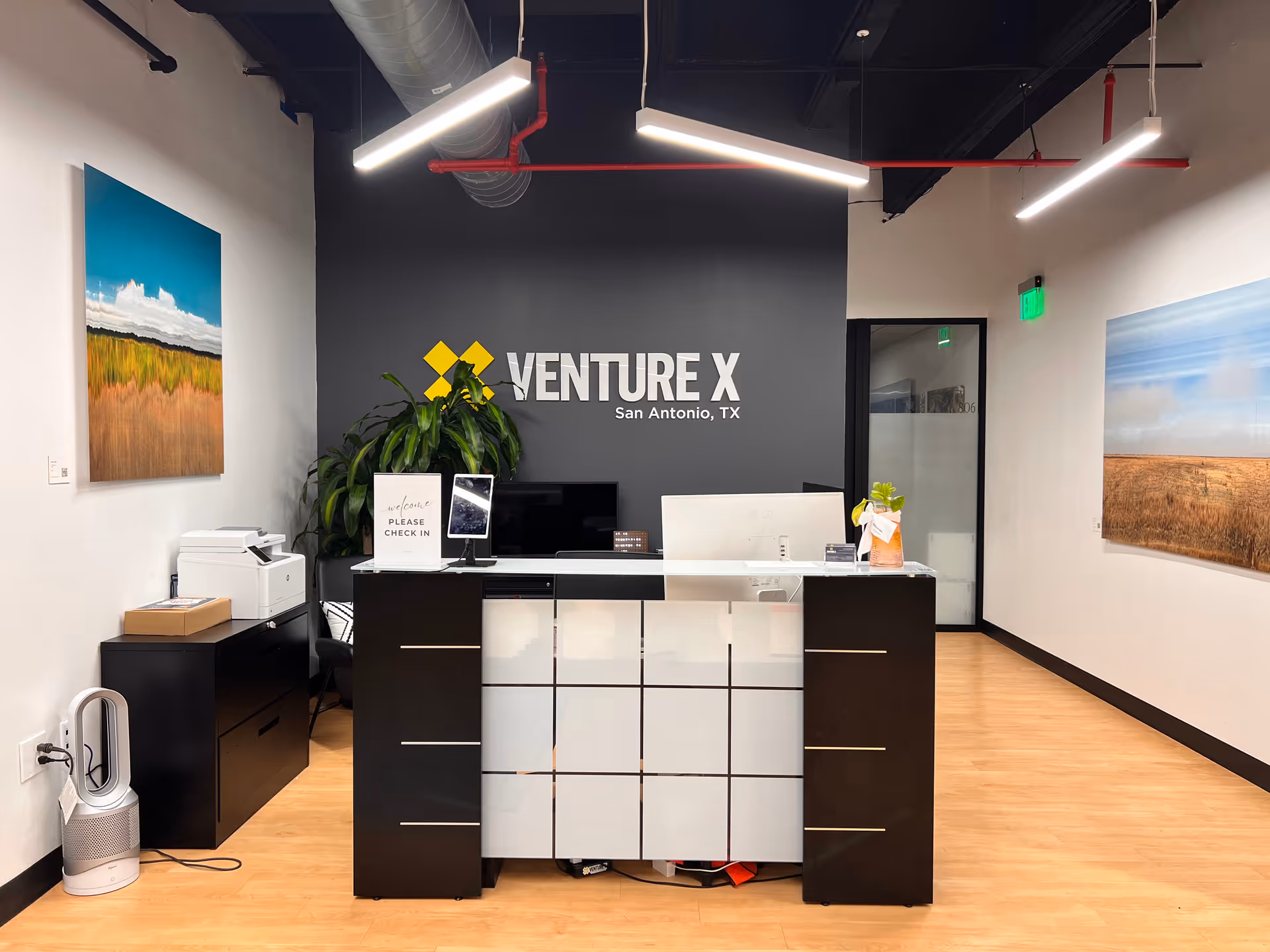 Reception desk in a modern coworking space with Venture X branding on a dark wall