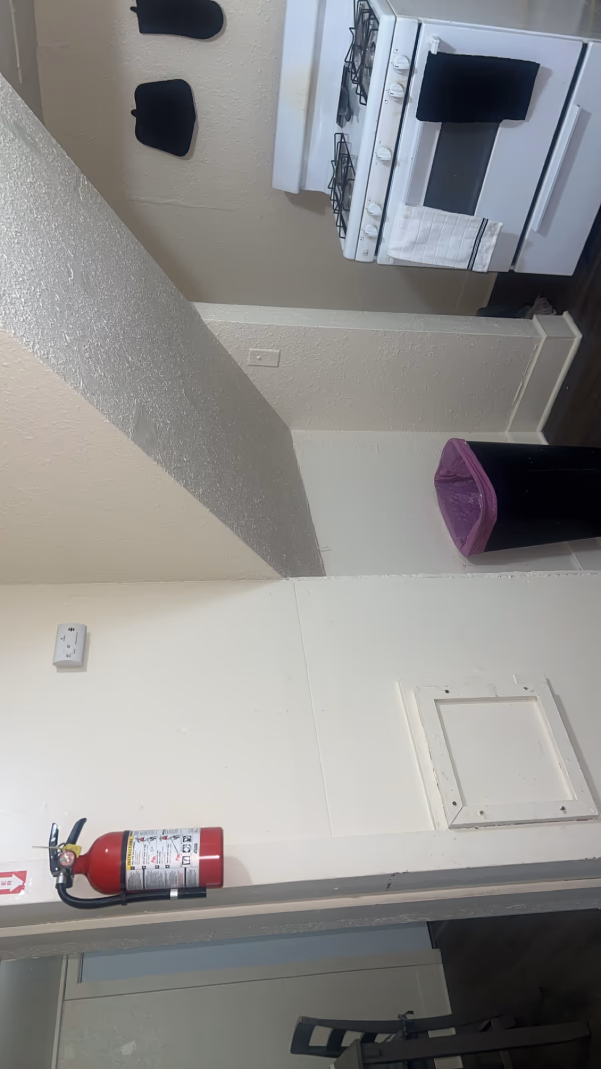 Interior kitchen area with stove, purple trash can, and a fire extinguisher.