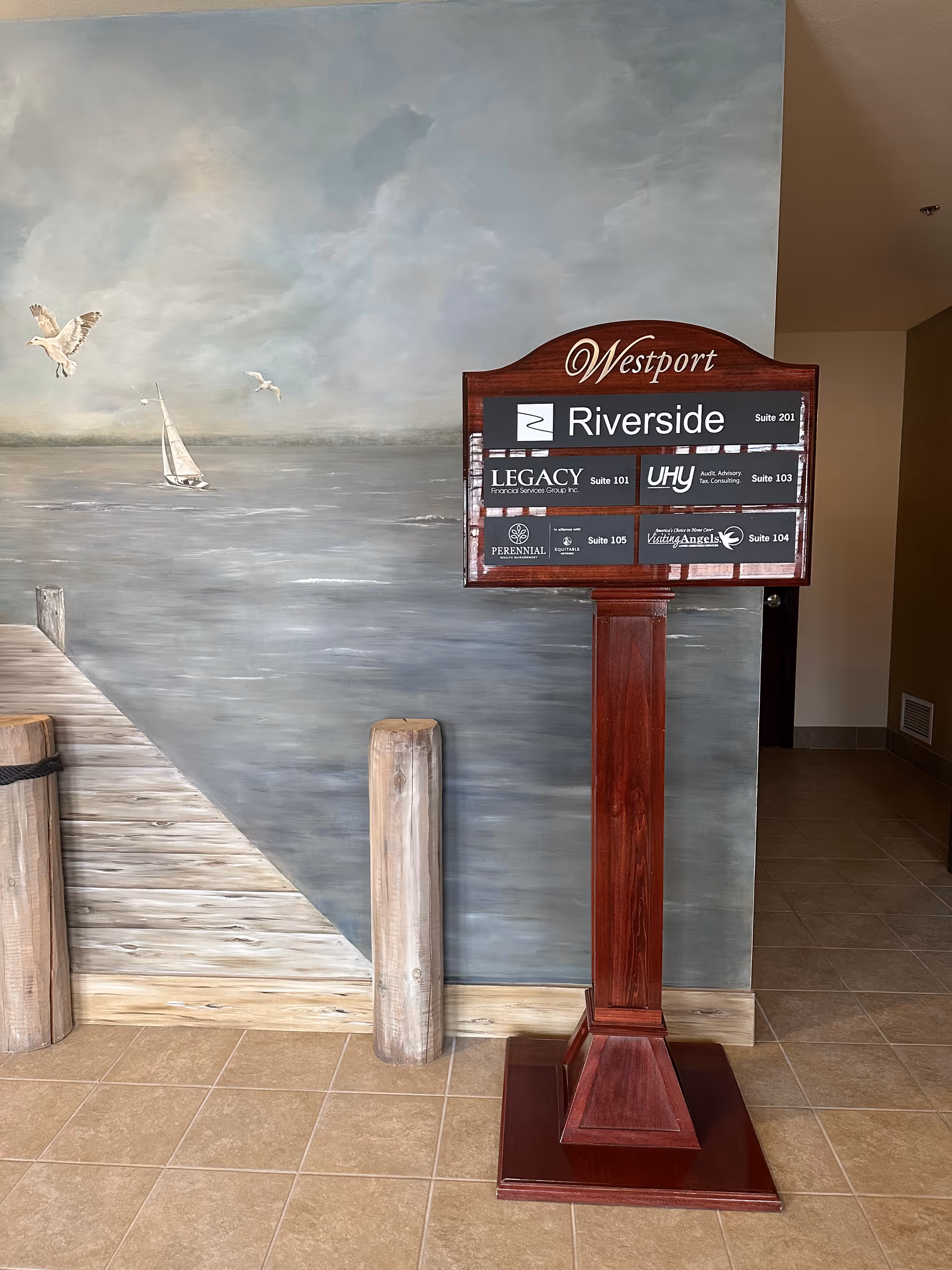 A tall wooden directory sign in a mural-decorated interior hallway.
