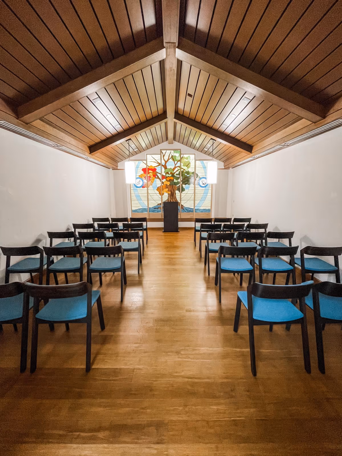 Rows of blue chairs face a stained-glass tree artwork in a central front room.