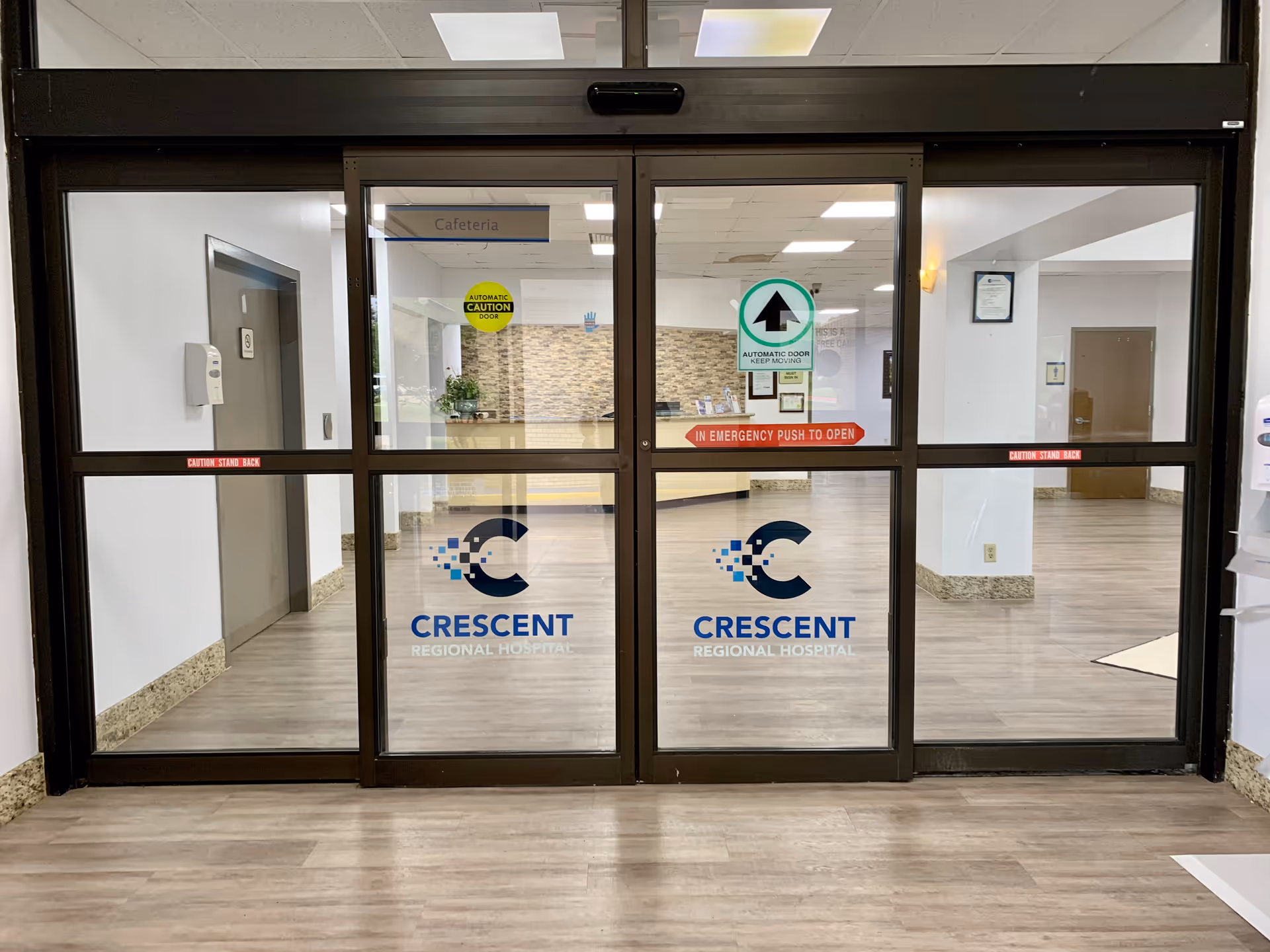 Glass entrance doors with Crescent Regional Hospital logos inside a hospital lobby.