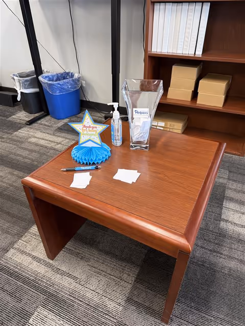 A wooden reception desk with hand sanitizer, a star award, and brochures in an office area.
