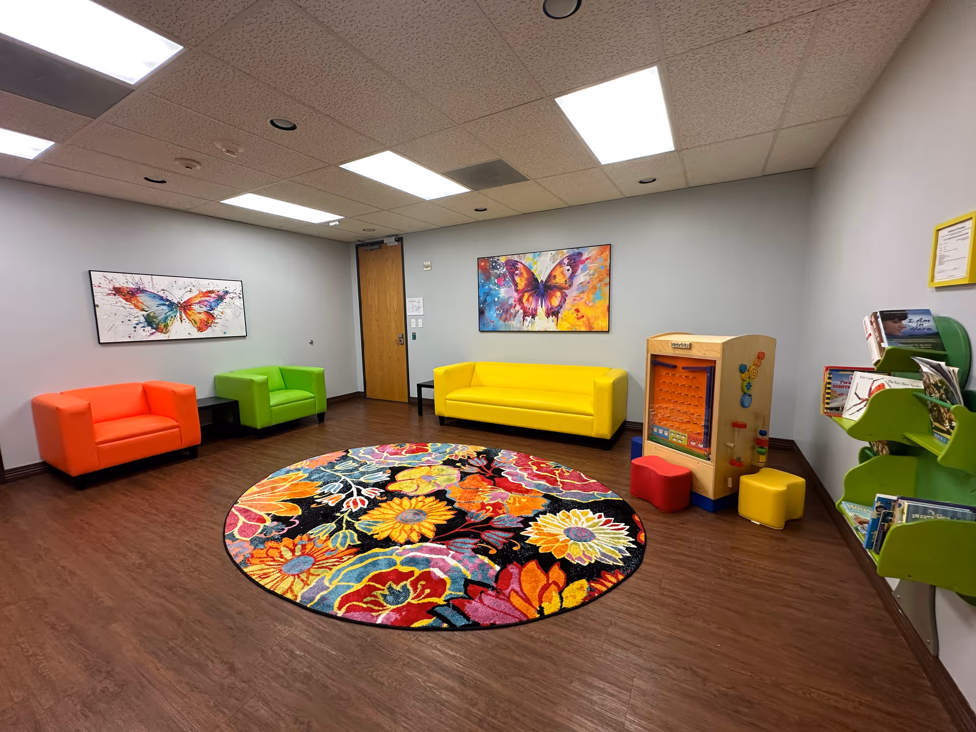 Colorful lounge area with bright couches, a circular rug, and butterfly artwork.