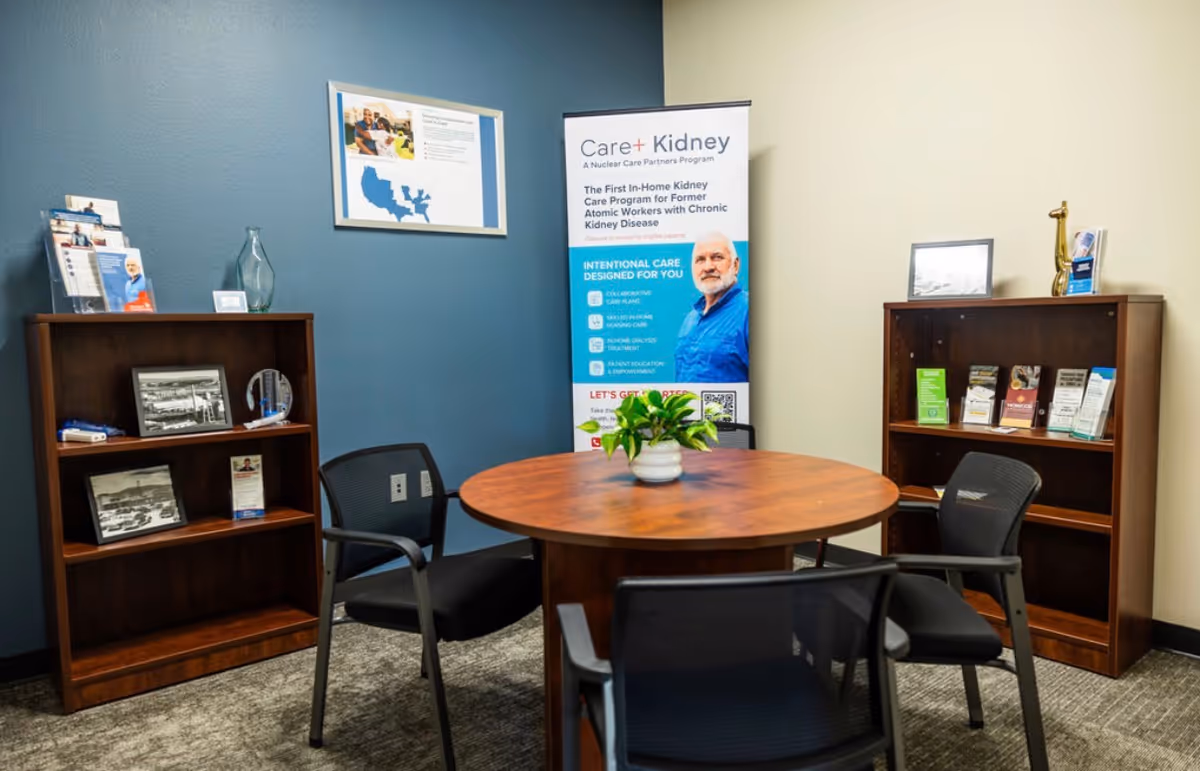 Round wooden table with black chairs in a small lobby, flanked by bookcases and a banner.