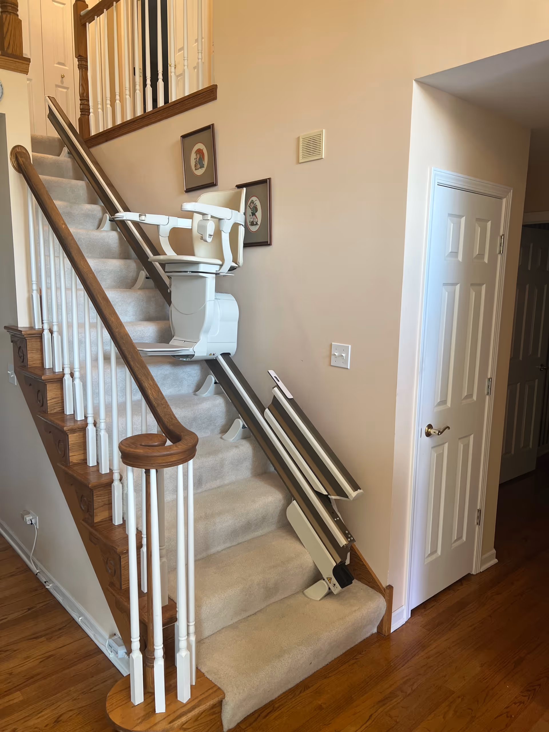 Indoor stairwell with a white stairlift attached to carpeted stairs and railing.
