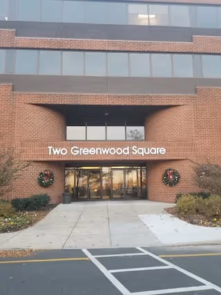 Brick exterior of Two Greenwood Square, glass doors at entrance with wreaths and trimmed shrubs.