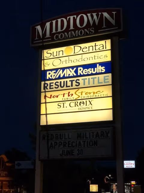Nighttime exterior signboard for Midtown Commons with St. Croix Hospice and other businesses.