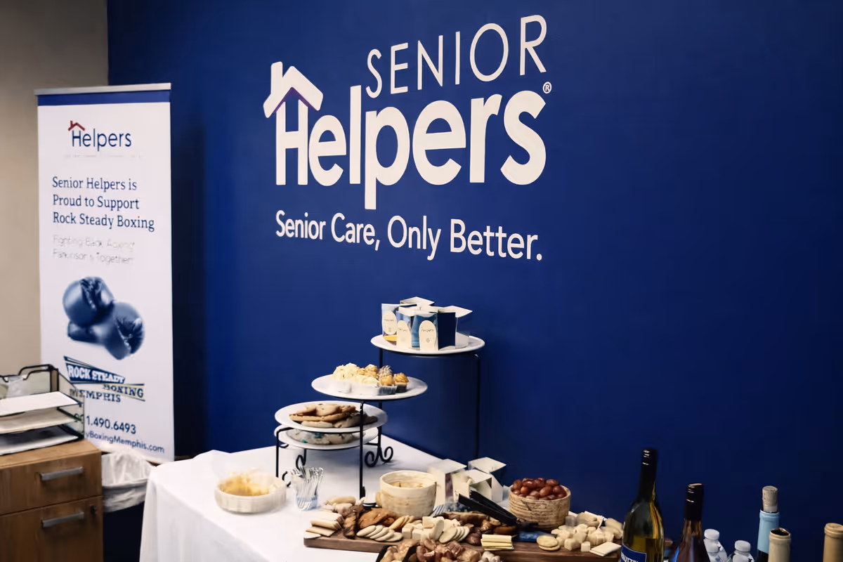Blue wall with Senior Helpers branding and a table of snacks and drinks.