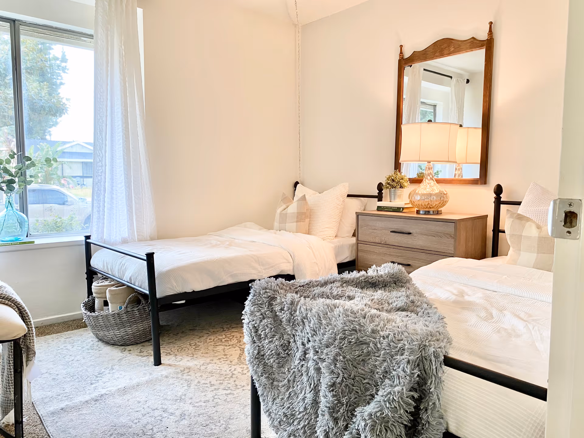 Two single beds with white bedding and a wooden dresser with mirror in a bright bedroom.