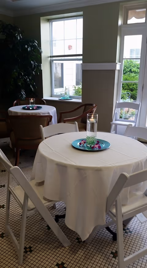 A bright dining room with round tables, white chairs, and candle centerpieces.