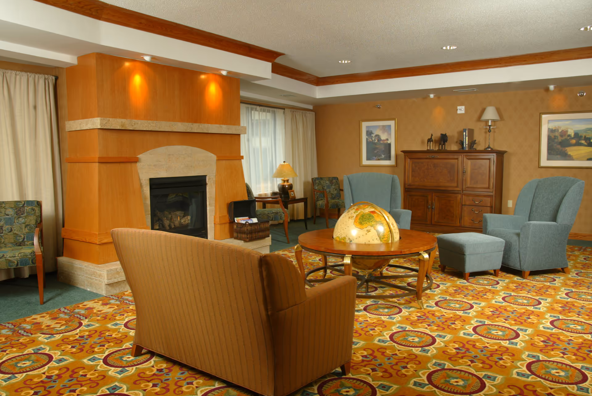 Cozy lounge with a fireplace, colorful patterned carpet, and seating around a globe table.