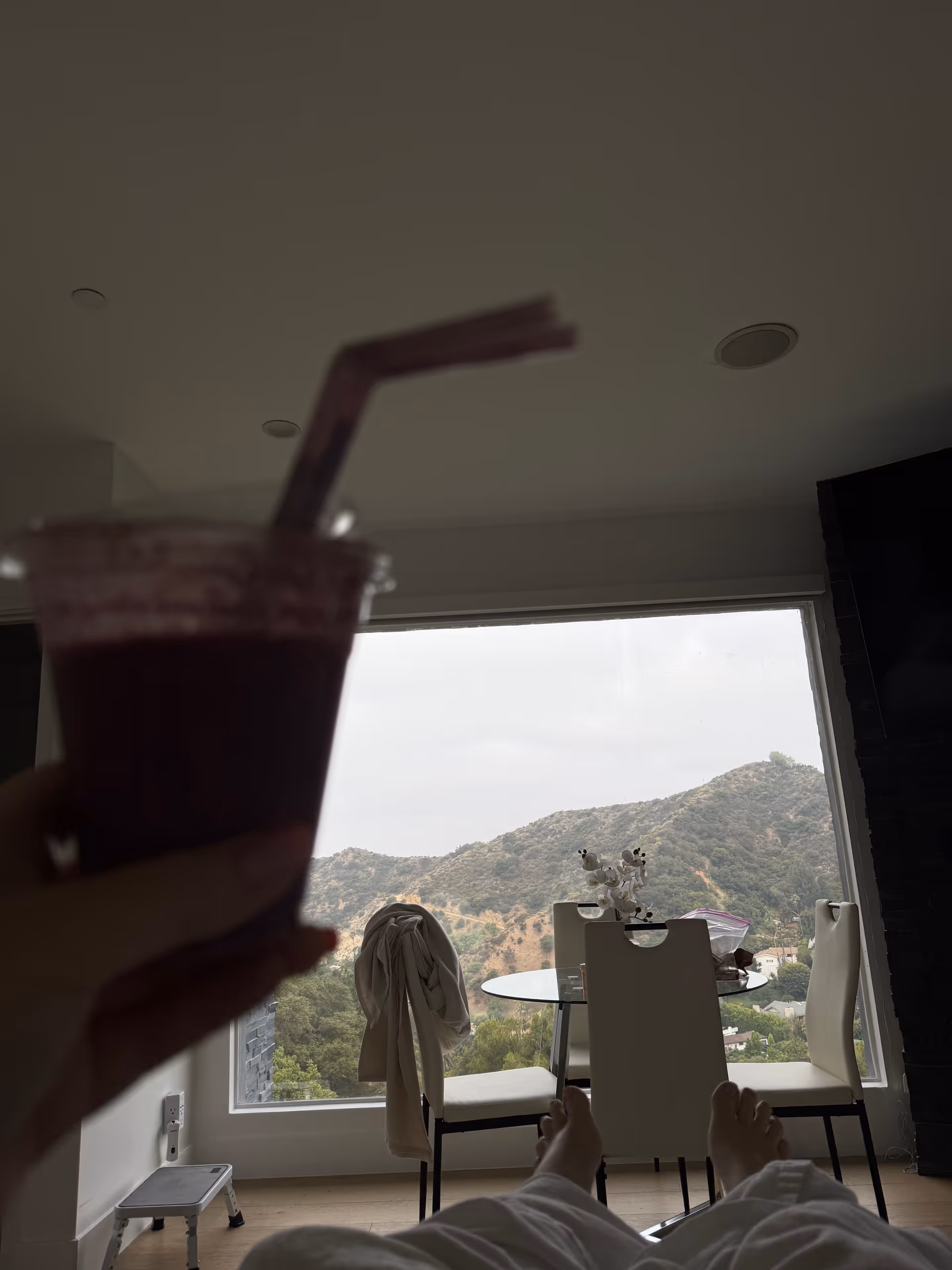 A resident's legs visible in a bright living area with a glass table and mountain view.
