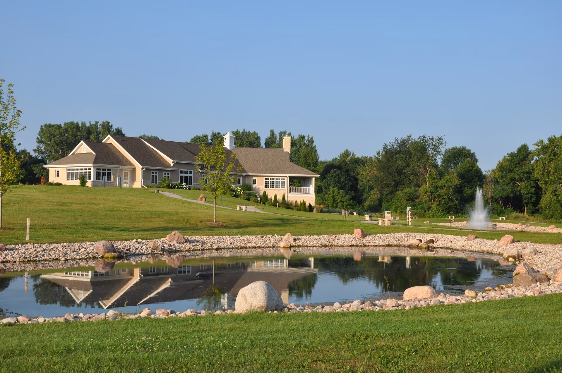 Exterior view of a single-story building with a pond, fountain, and green lawn.