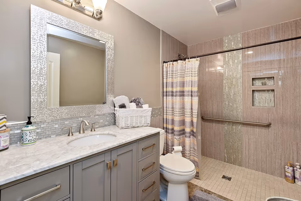 Grey bathroom with marble vanity, large mirror, toilet, shower with curtain, basket of towels.