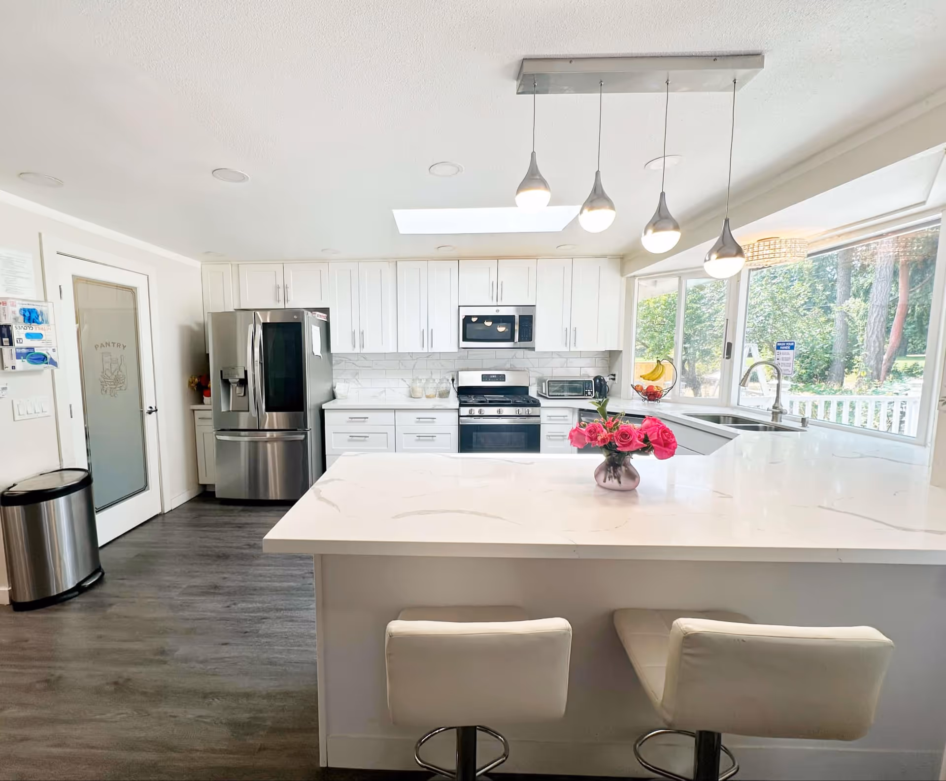 Bright, modern kitchen with white cabinets, island, stainless appliances, and large window.
