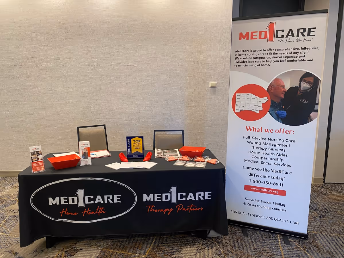 Indoor conference setup with a Med1Care table, promotional banner, and informational materials.