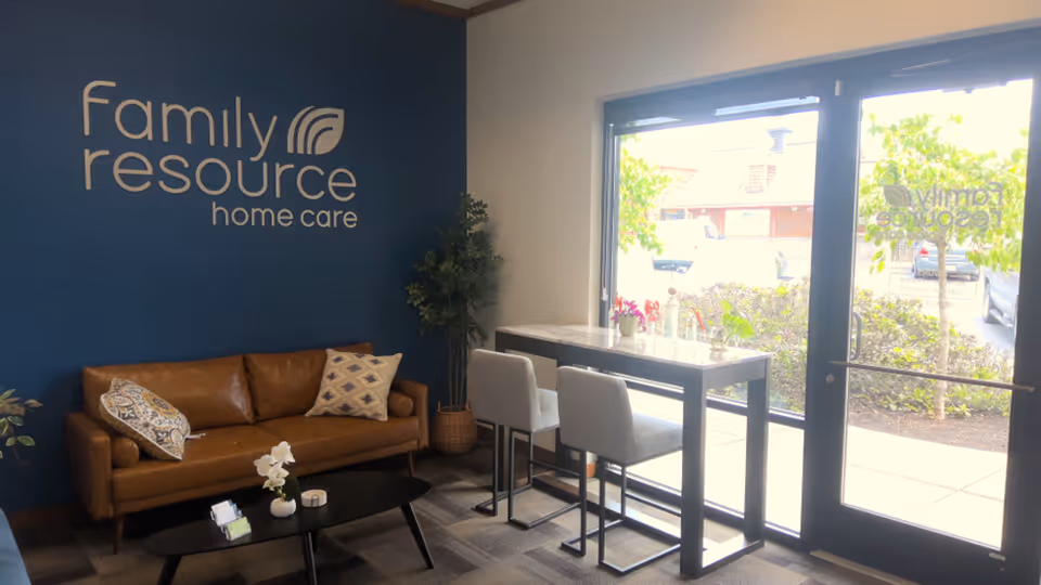 Lobby area with blue wall logo, brown sofa, and glass doors by a high table.
