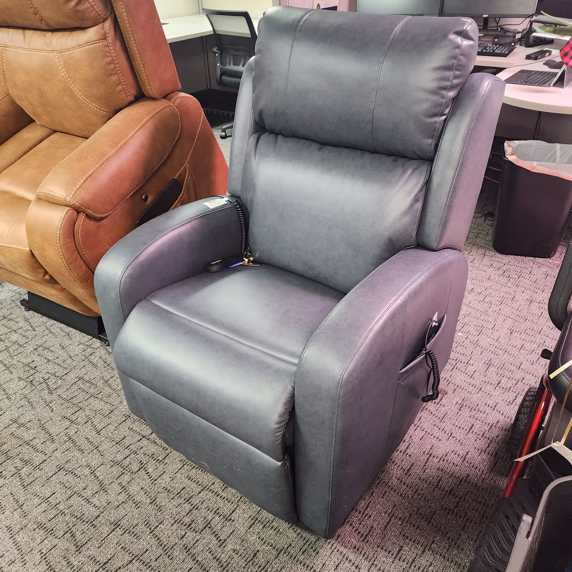 Gray leather recliner chair in a showroom with other seating and desks.