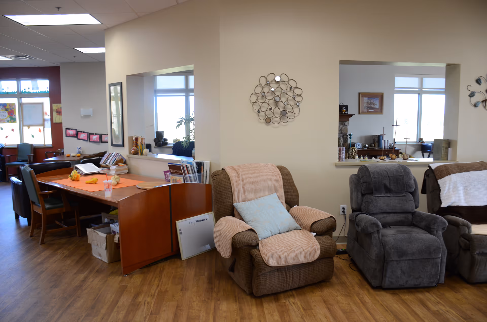 A spacious senior center lounge with recliner chairs, a desk, and warm wood floors.