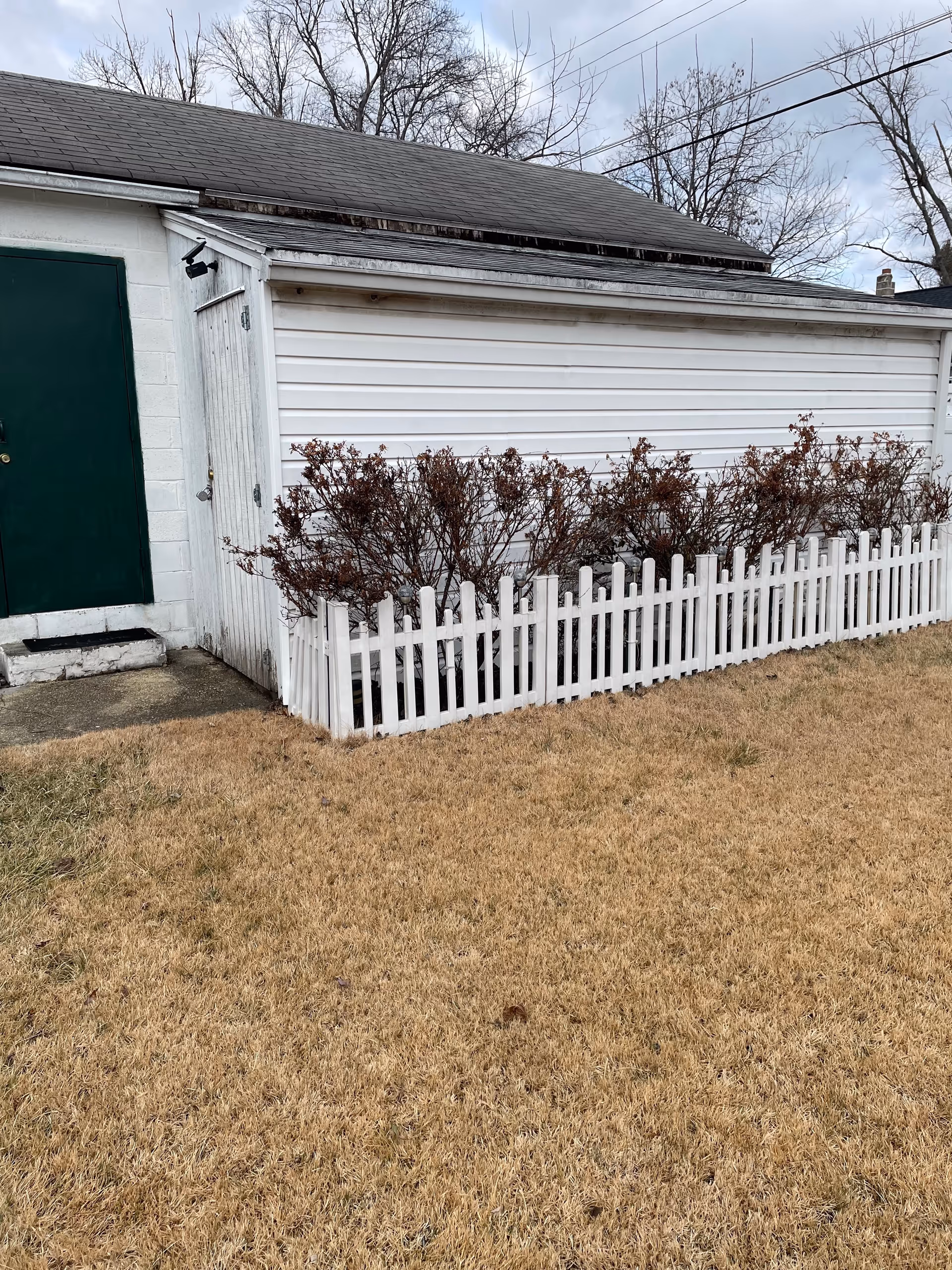 Outdoor view of a white building with a green door, shrubs, and a white picket fence.