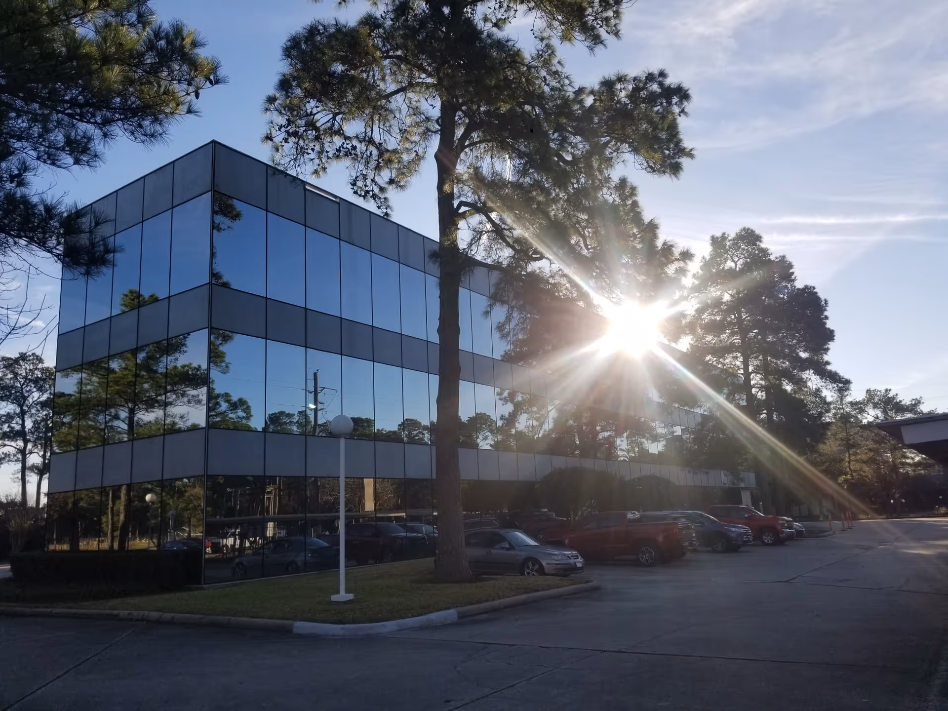 Glass-front office building with sun glare and parked cars in a lot